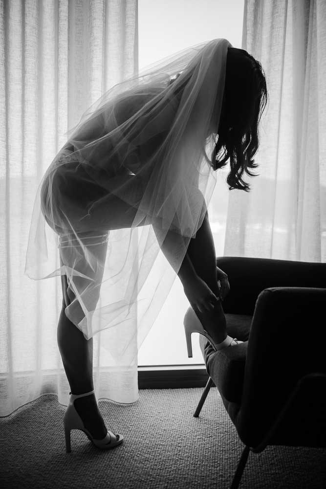 Bride taking boudoir photo session through window light in black and white